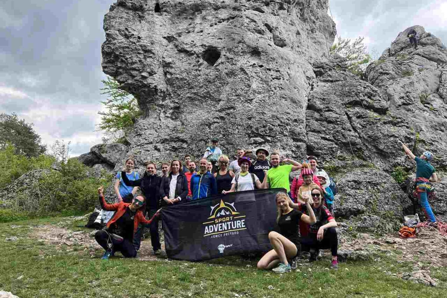 Grupa uczestników wyprawy Sport Adventure z banerem na tle wapiennych skał Jury Krakowsko-Częstochowskiej.