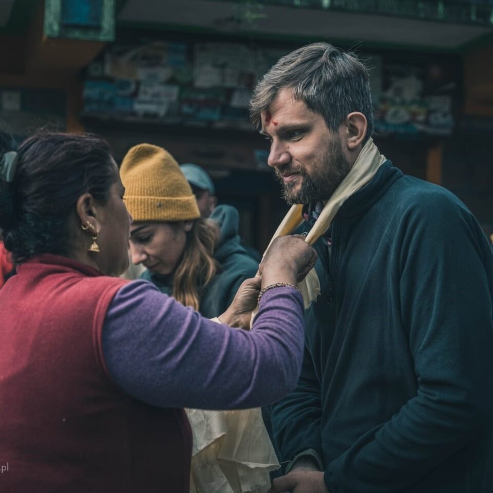 Powitanie podróżnika tradycyjnym szalem w nepalskiej wiosce podczas trekkingu w Himalajach.