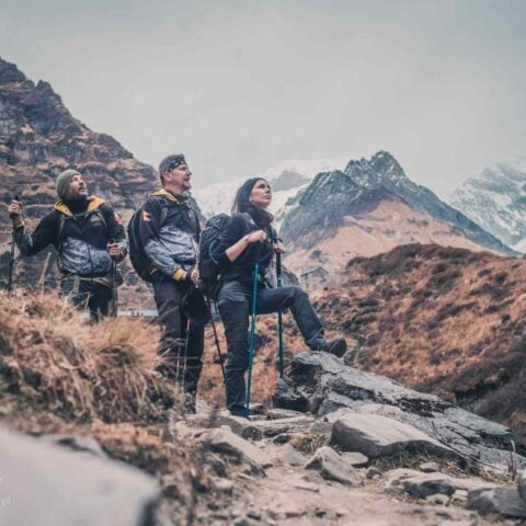 Trójka uczestników trekkingu w Nepalu podziwia widok na ośnieżone szczyty Annapurny w Himalajach.