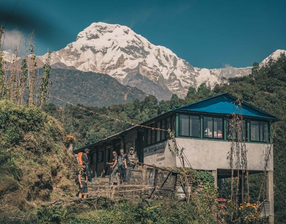 Trekkerzy przed lodge w Himalajach z widokiem na ośnieżony szczyt Annapurna South w Nepalu.