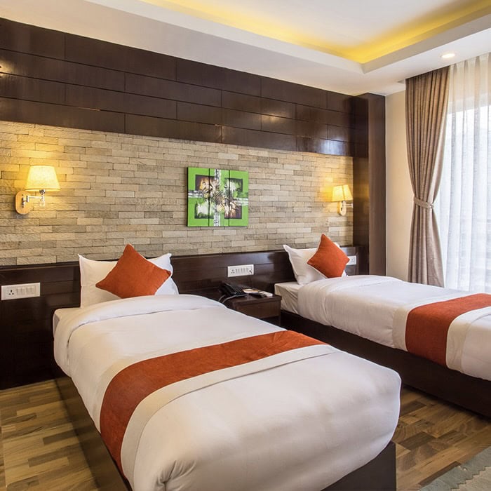 Nowoczesny pok&oacute;j hotelowy z dwoma pojedynczymi ł&oacute;żkami, białą pościelą i pomarańczowymi akcentami.