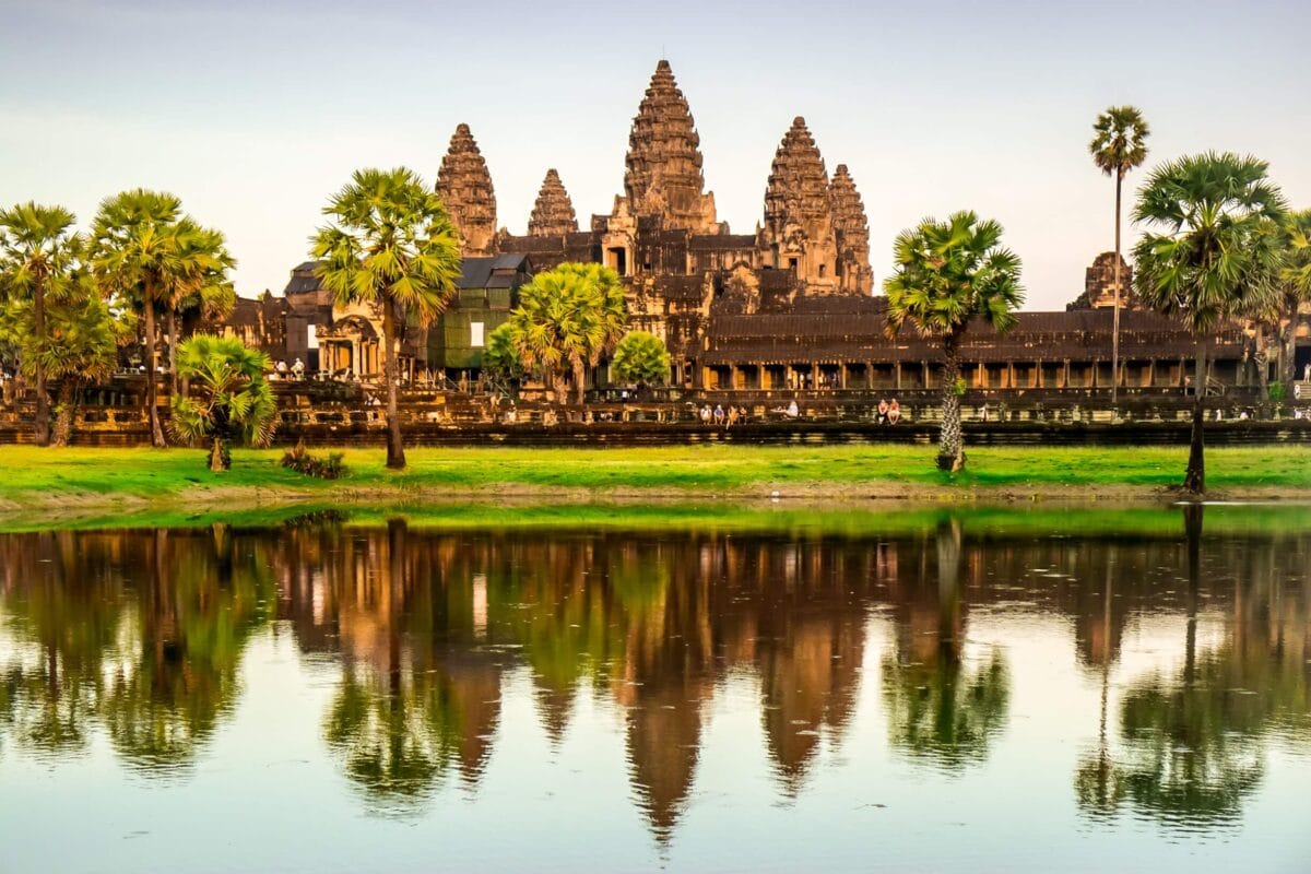 Świątynia Angkor Wat w Kambodży w świetle dziennym, z palmami i odbiciem w wodzie na pierwszym planie.