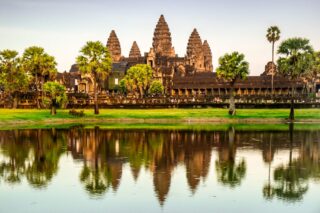 Świątynia Angkor Wat w Kambodży w świetle dziennym, z palmami i odbiciem w wodzie na pierwszym planie.