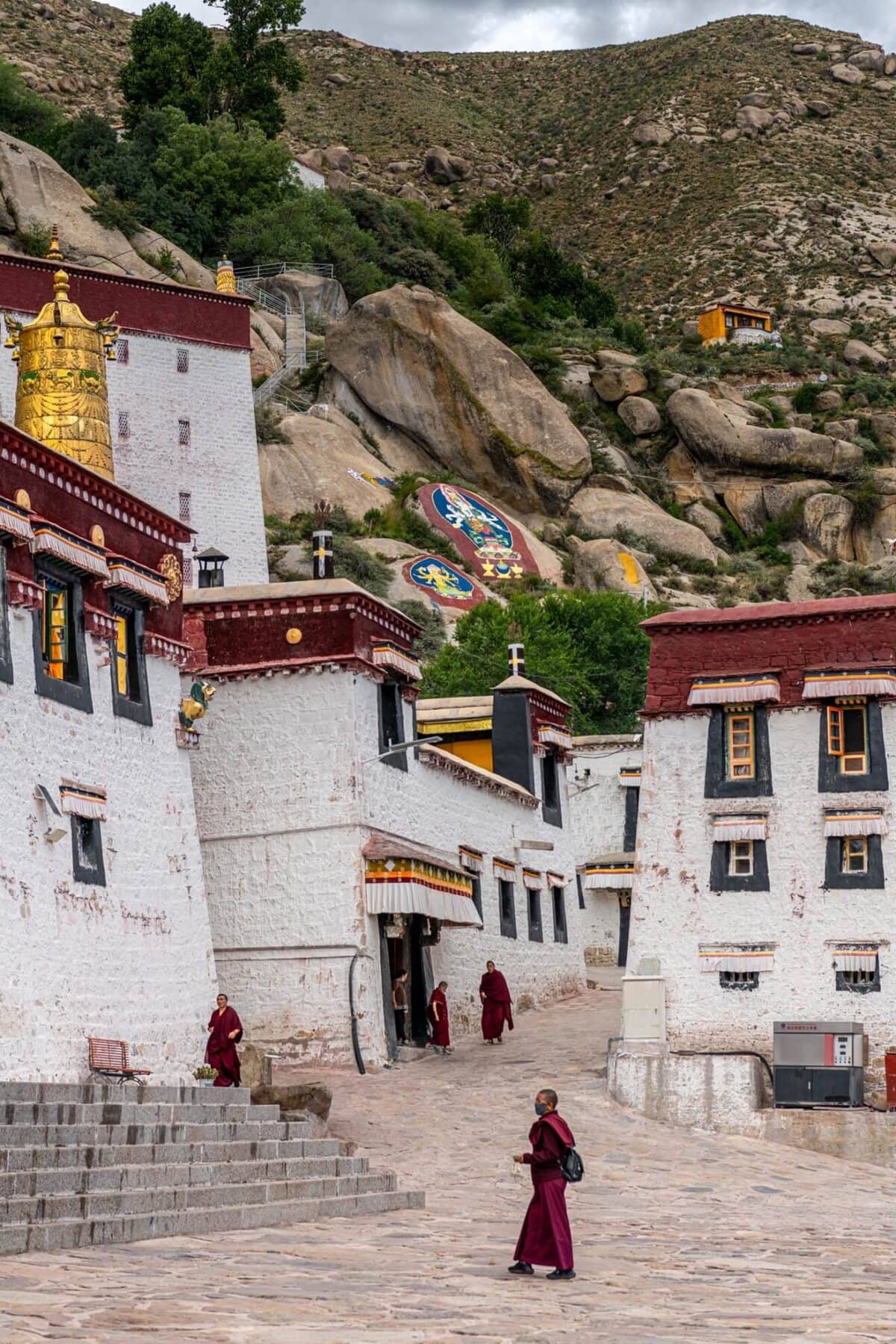 Klasztor Sera Lhasa Tybet – mnisi tybetańscy spacerujący po dziedzińcu białych murów z czerwonymi detalami, w tle skaliste wzgórza