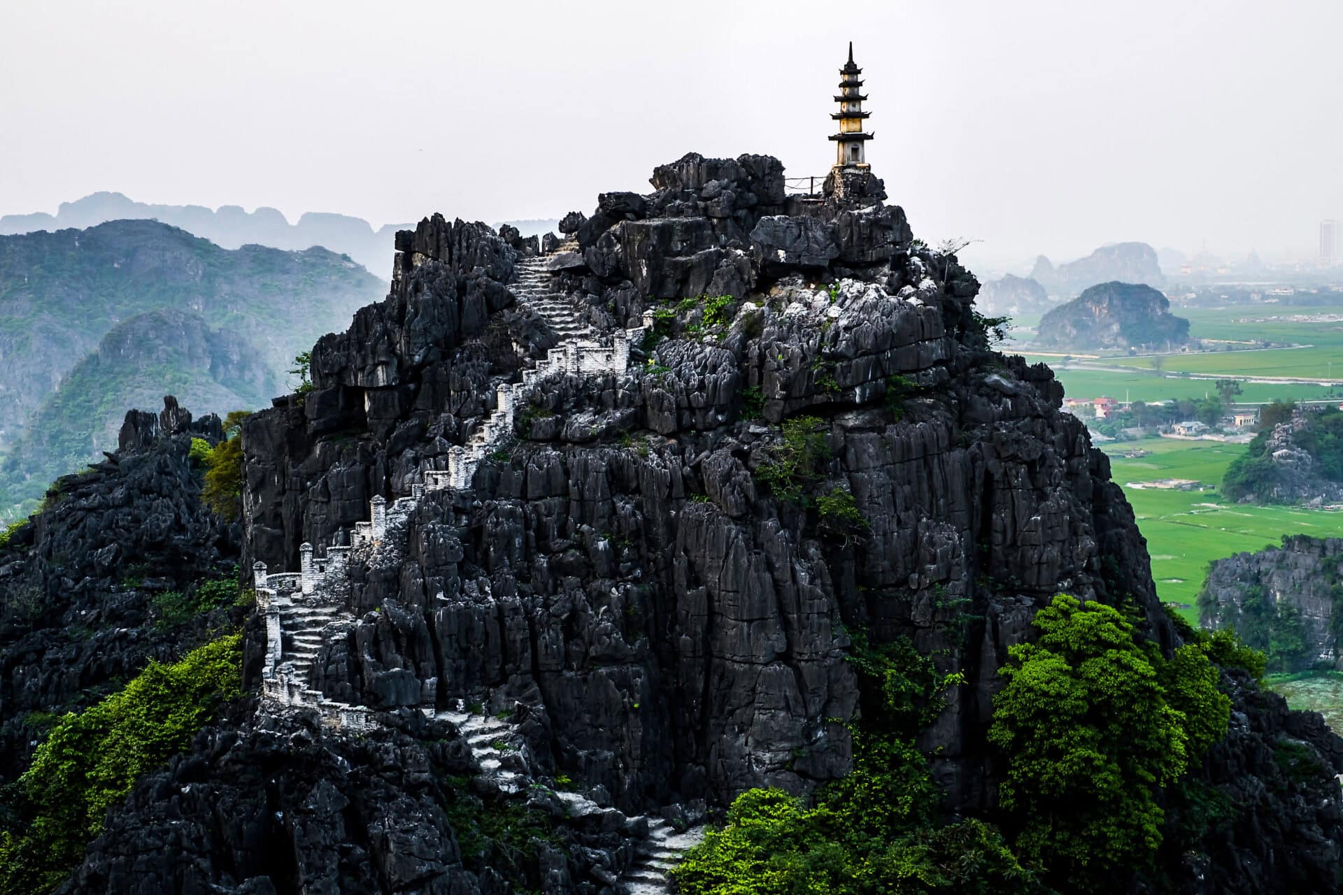 Góra w punkcie widokowym Jaskinia Mua w Ninh Binh, Wietnam. Strome, kręte białe schody wspinają się po ciemnej, skalistej formacji.