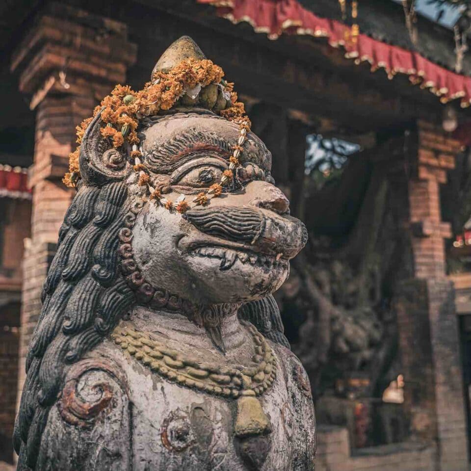Kamienna figura lwa z girlandą z kwiatów przy hinduistycznej świątyni w Nepalu.