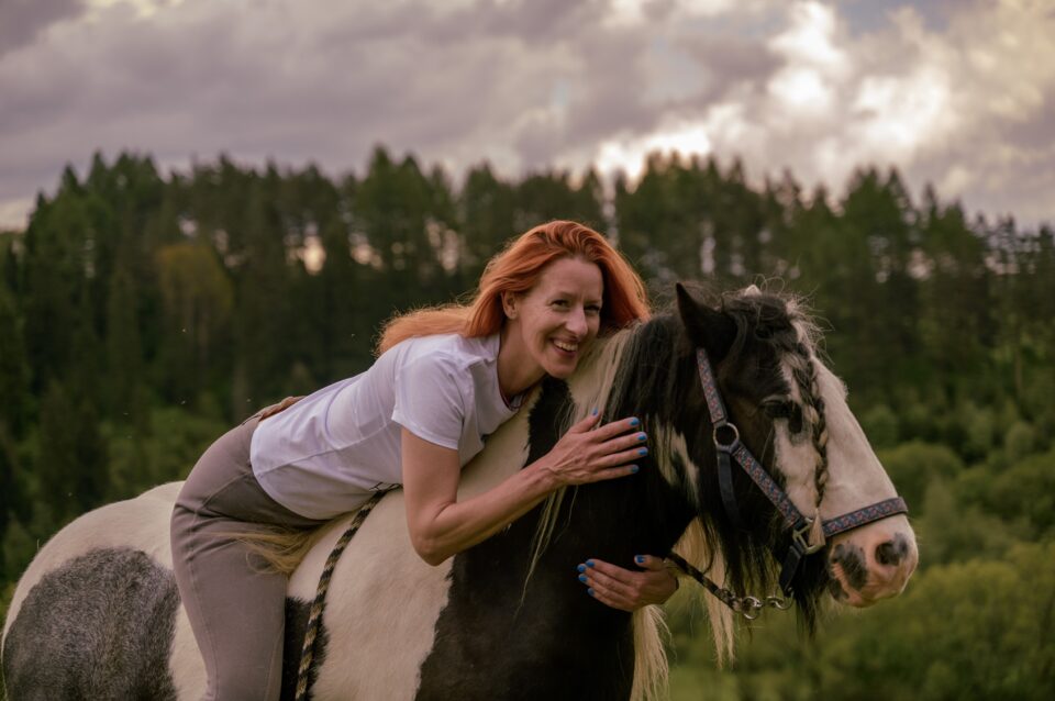 Kobieta o rudych włosach leży na grzbiecie srokatego konia w Bieszczadach