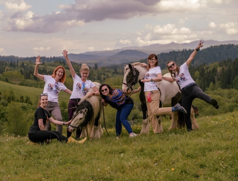 Grupa uśmiechniętych kobiet z końmi na łące w Bieszczadach – kobiecy wyjazd z jazdą konną i panoramą gór w tle.