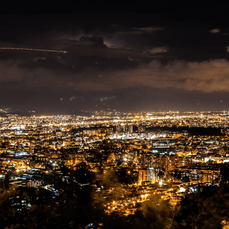 Widok na Bogotę nocą z góry Monserrate, miasto rozświetlone tysiącami świateł pod dramatycznym niebem.