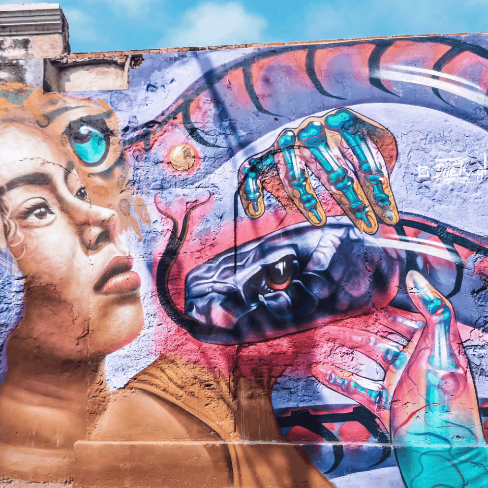Kolorowy mural na ścianie budynku w Cartagenie przedstawiający kobietę, węża i szkieletową dłoń – pełen symboliki i kontrastów uliczny street art.