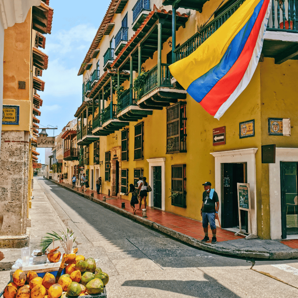 Kolorowa ulica w historycznym centrum Cartageny, z balkonami zdobionymi zielenią i powiewającą kolumbijską flagą, na tle kolonialnych budynków.