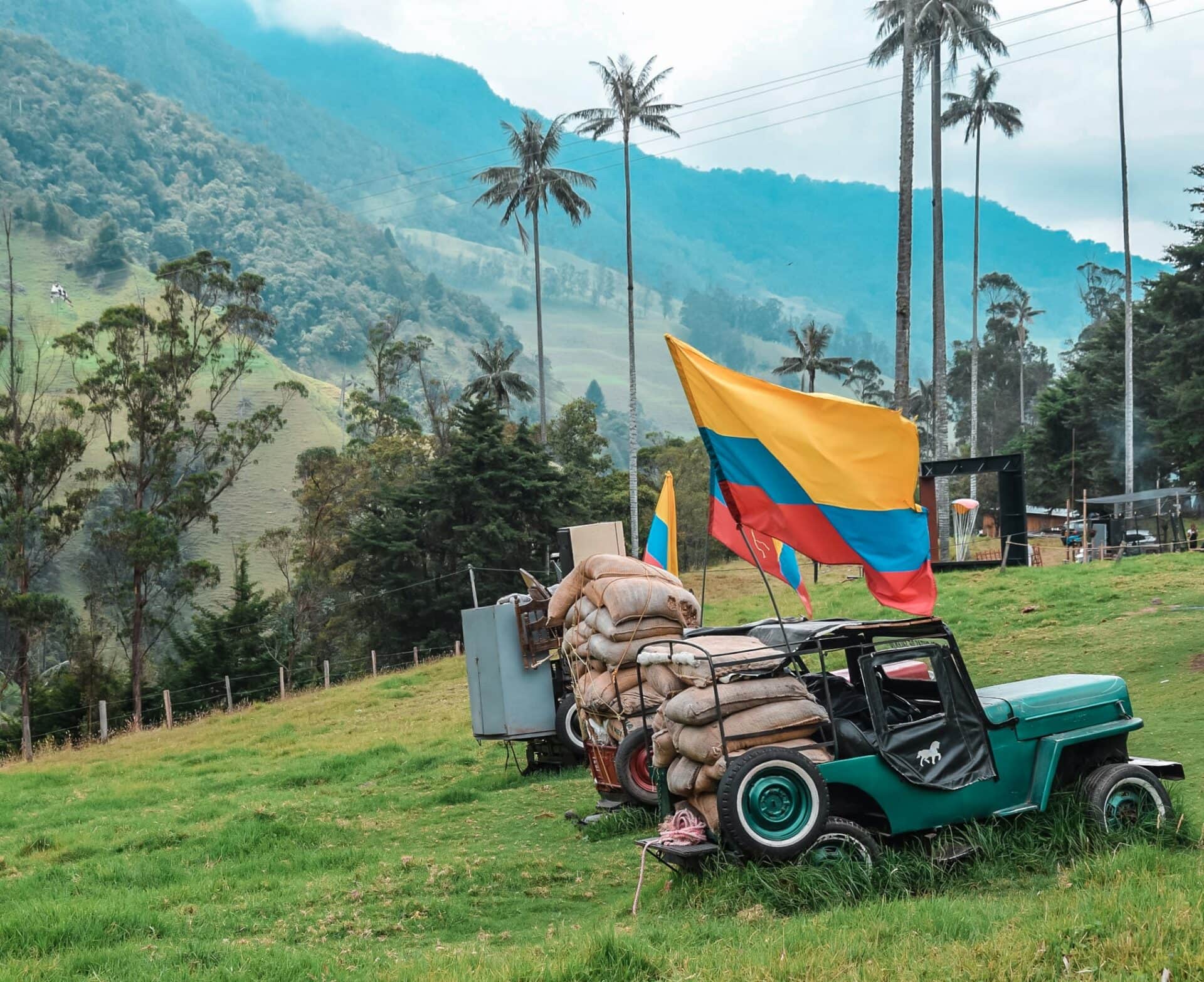 Tradycyjny jeep z workami kawy i flagą Kolumbii na tle zielonych wzgórz i najwyższych na świecie palm woskowych w Dolinie Cocora.