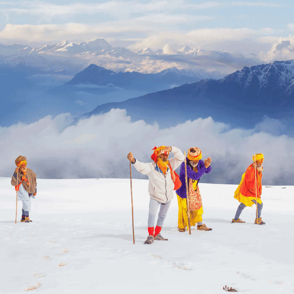 Czterech starszych mężczyzn w tradycyjnych strojach i turbanach wędruje przez pokryty śniegiem krajobraz. Trzymają kijki, a w tle widać pasma górskie częściowo zasłonięte chmurami.