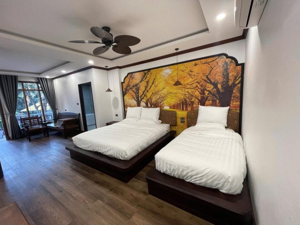 Pok&oacute;j w Dream1985 Hotel w Laosie z dwoma pojedynczymi ł&oacute;żkami, drewnianą podłogą i jesienną grafiką na ścianie.