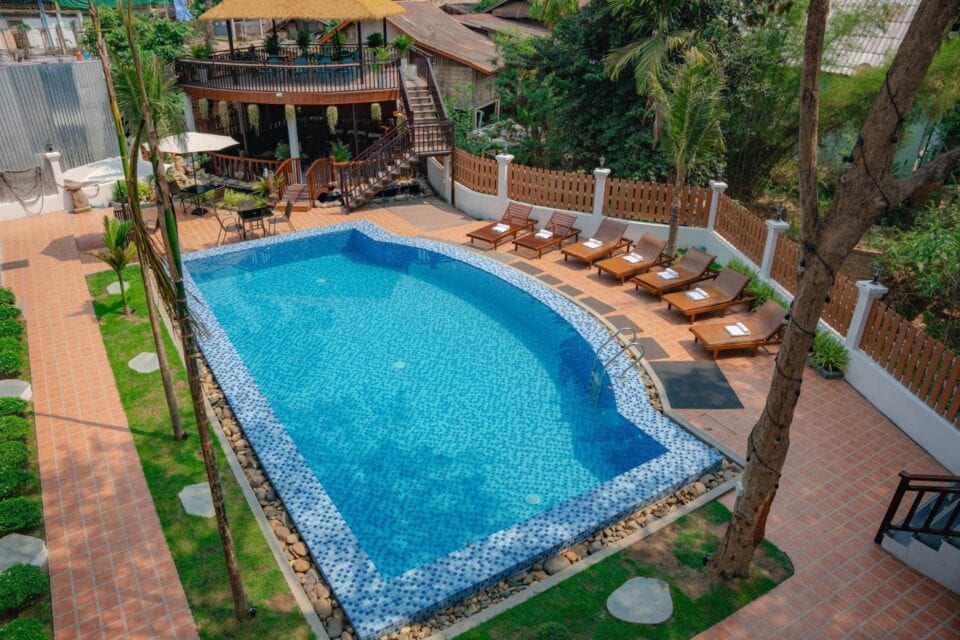 Basen zewnętrzny w Dream1985 Hotel w Laosie otoczony leżakami i tropikalną roślinnością.