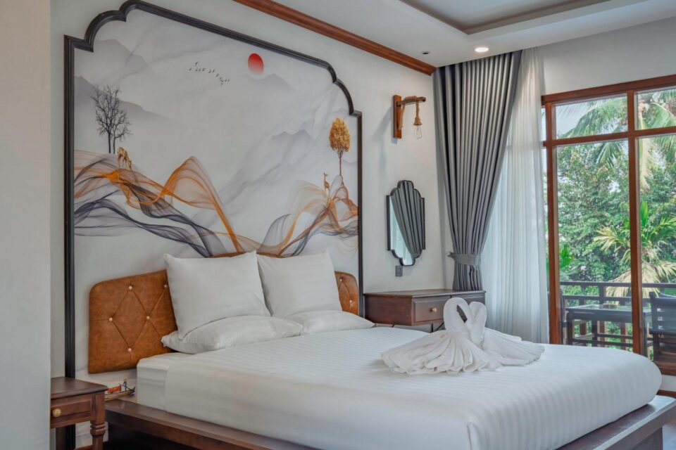 Pok&oacute;j hotelowy w Dream1985 Hotel w Laosie z dużym ł&oacute;żkiem, ozdobną grafiką na ścianie i widokiem na zieleń za oknem.
