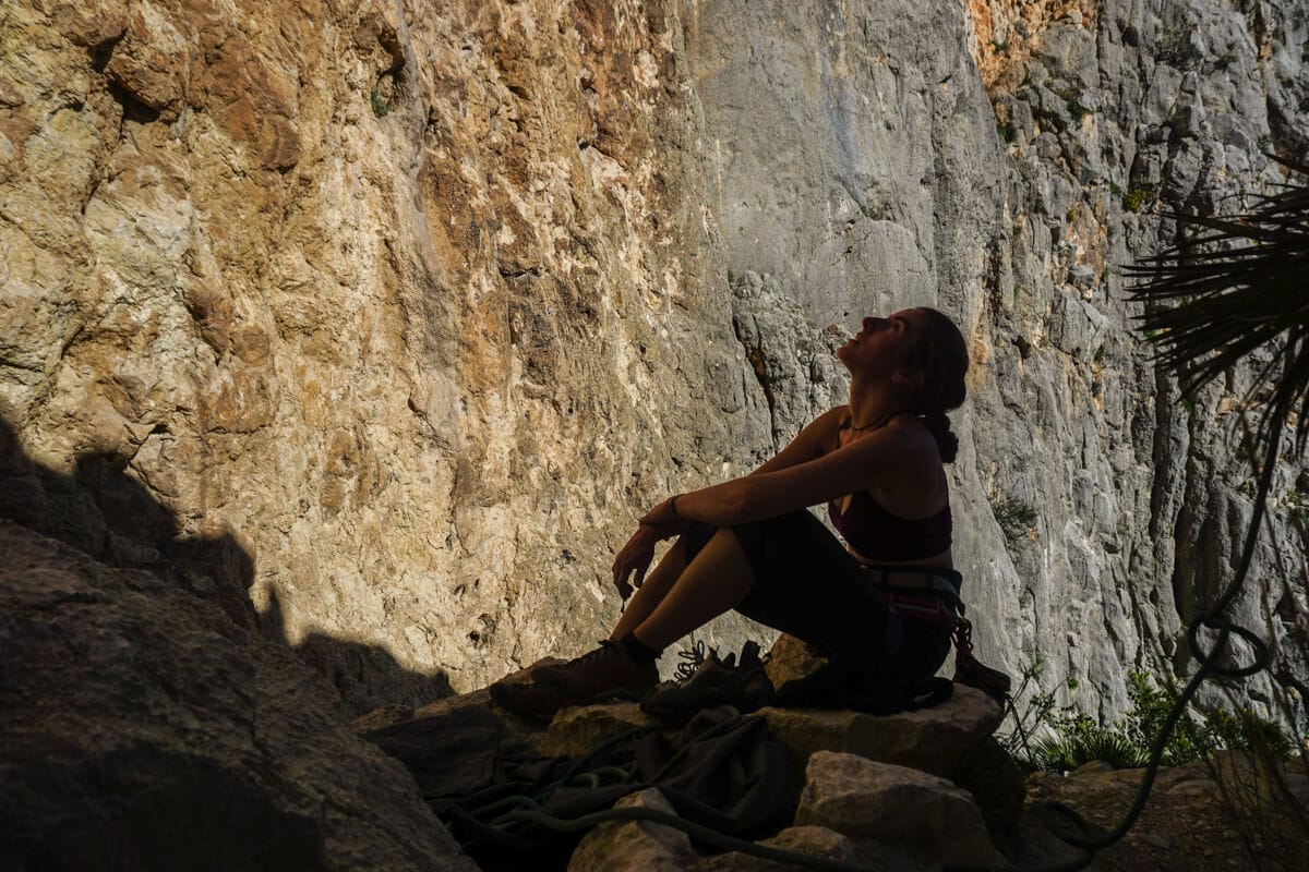 Kobieta siedzi w cieniu skał, patrzy w niebo