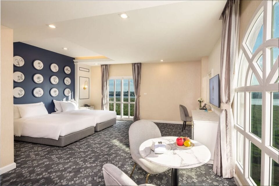 Nowoczesny pok&oacute;j hotelowy w Eastin Hotel Vientiane w Laosie, z dwoma dużymi ł&oacute;żkami, eleganckim wystrojem i widokiem na miasto przez panoramiczne okna.