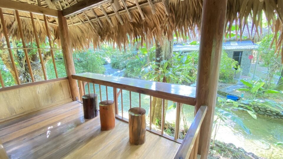 Taras bambusowej chatki w wiosce Hieu w Pu Luong z widokiem na tropikalną zieleń i strumień.