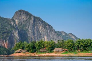 Wejście do jaskiń Pak Ou w Laosie – widok od strony rzeki Mekong, z wapiennym klifem i tropikalną roślinnością u podnóża.