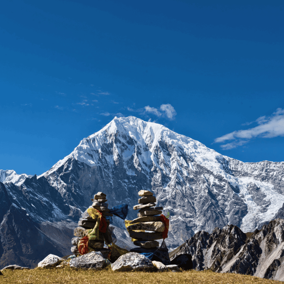Stos kamieni (chorten) z buddyjskimi flagami modlitewnymi na tle majestatycznego, ośnieżonego szczytu Langtang Lirung w Dolinie Langtang w Nepalu.