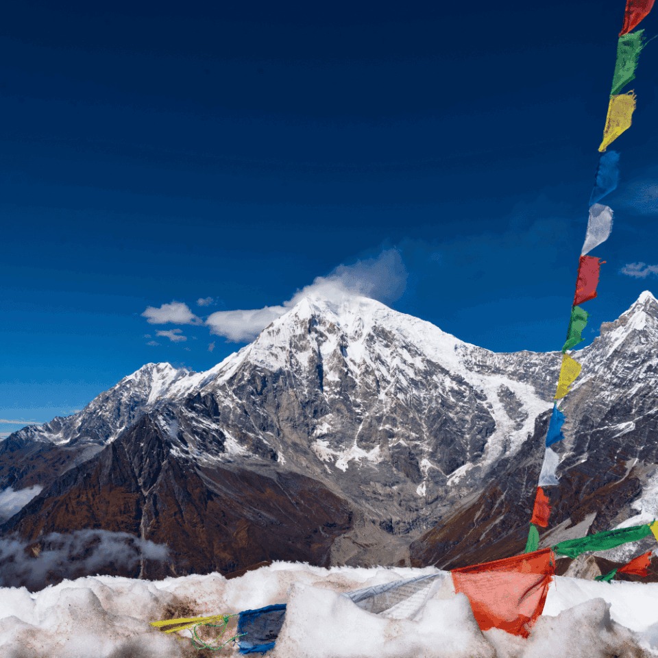 Kolorowe buddyjskie flagi modlitewne powiewające nad zaśnieżonym zboczem z ośnieżonym szczytem Langtang Lirung w tle, widok z trekkingu w Dolinie Langtang.