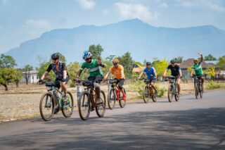 Grupa rowerzystów na trasie wyprawy rowerowej przez Laos, z górskim krajobrazem w tle.