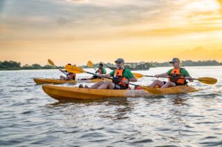 Turyści w kajakach na rzece Mekong o zachodzie słońca w Laosie.