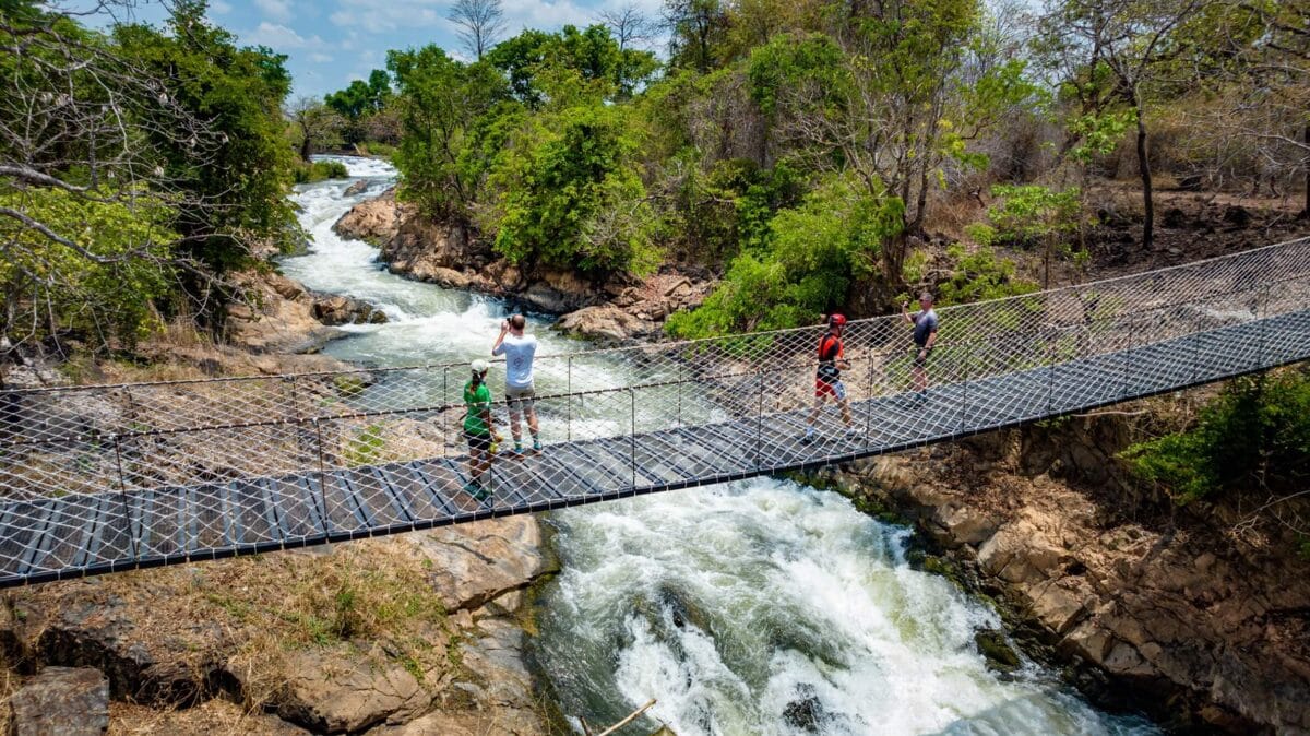 Turyści przechodzący przez wiszący most nad rwącą rzeką w Laosie.
