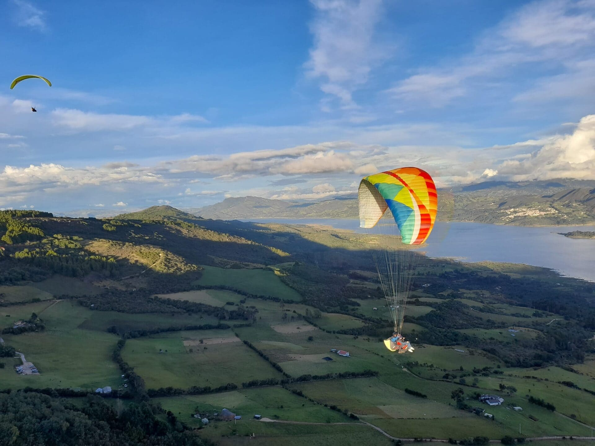 Kolorowy paralotniarz szybujący nad zielonymi wzgórzami i rzeką w kanionie Chicamocha.