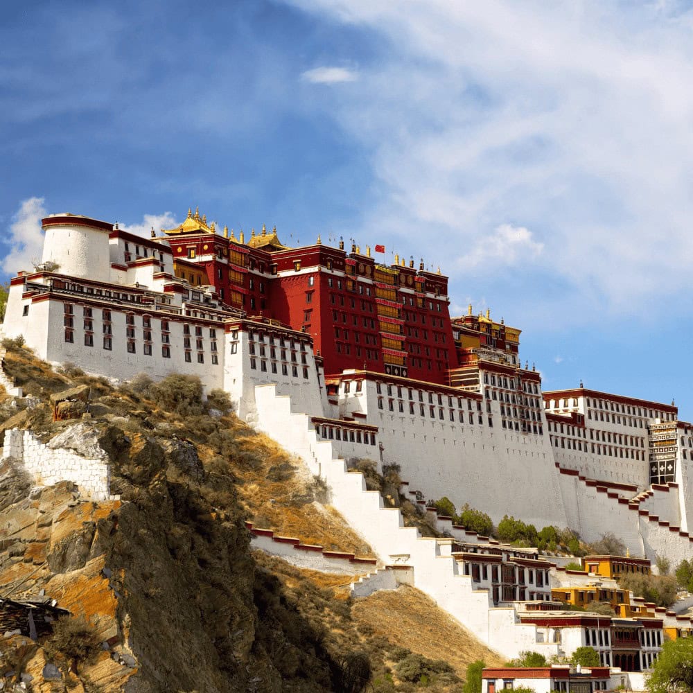 Monumentalny Pałac Potala w Lhasie, dawna siedziba Dalajlamów, wznoszący się na wzgórzu Marpo Ri. Białe i czerwone mury kompleksu kontrastują z błękitnym niebem i otaczającymi go surowymi, górzystymi krajobrazami Tybetu.