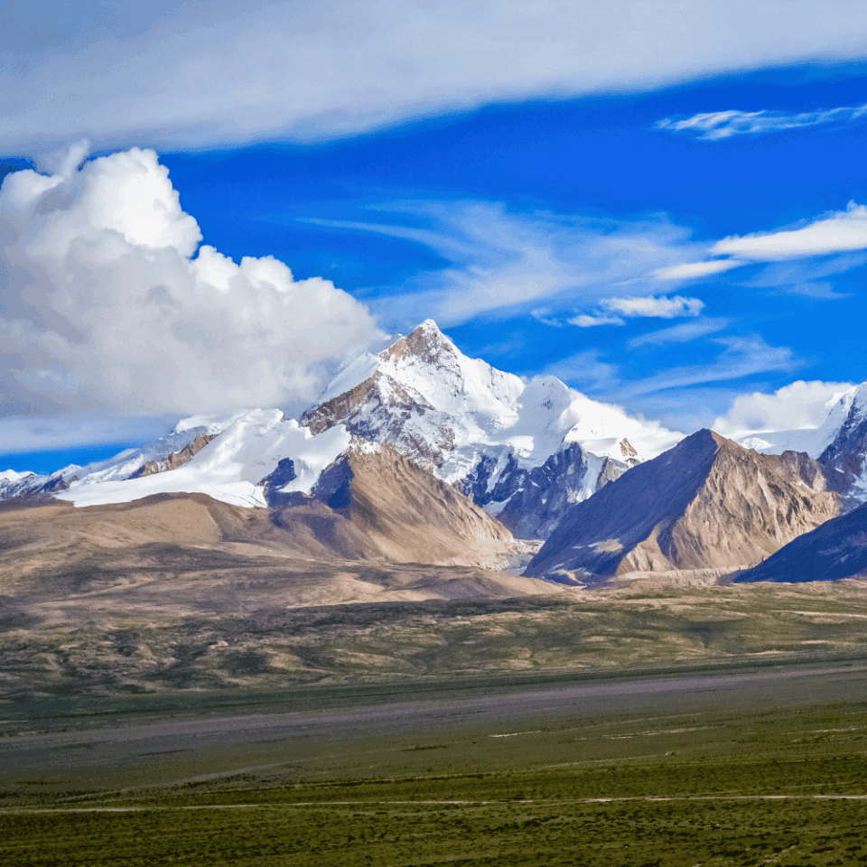 Rozległe pasmo ośnieżonych szczytów Himalajów w Parku Narodowym Langtang w Nepalu, z szeroką doliną i chmurami na tle błękitnego nieba.