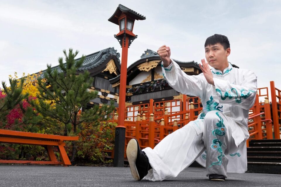 Mężczyzna wykonujący sekwencję tai chi na tle tradycyjnej wietnamskiej architektury.