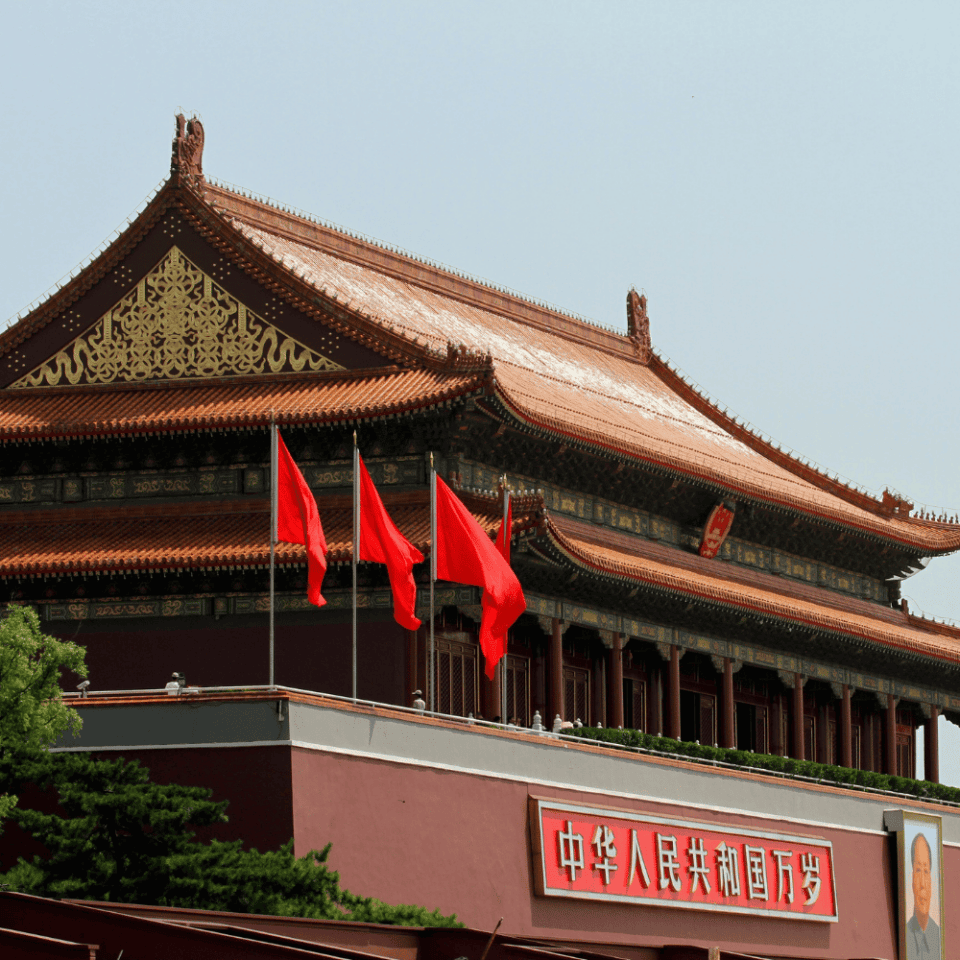Zbliżenie na dach i fasadę Bramy Niebiańskiego Spokoju ozdobionej czerwonymi flagami, symbol Pekinu i władzy państwowej.
