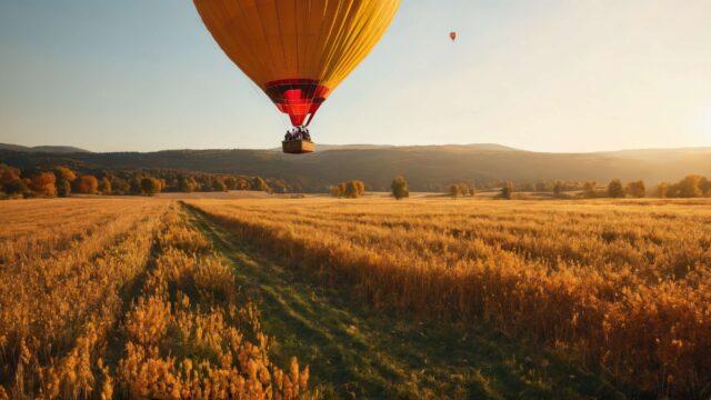 Balon na gorące powietrze unosi się nad złotym polem w jesiennym krajobrazie z widokiem na góry.