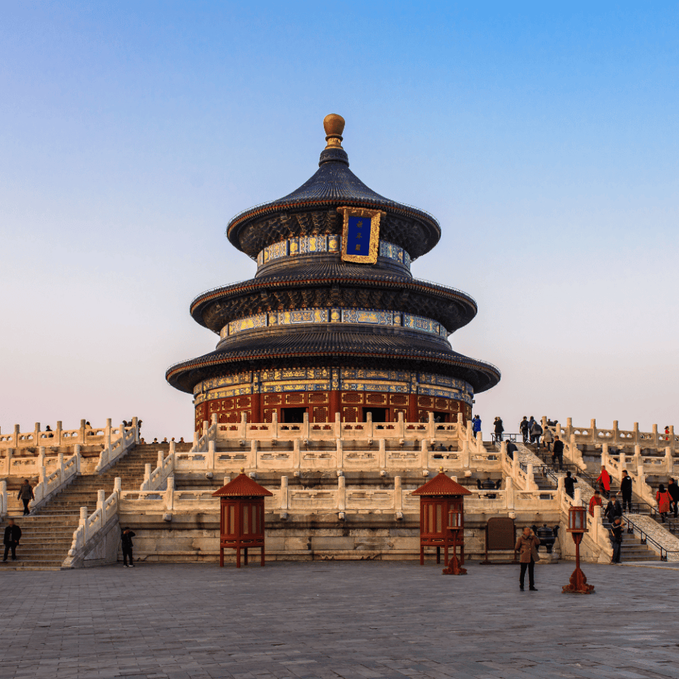 Widok na Świątynię Nieba w Pekinie – klasyczny okrągły budynek z niebieskim, dachowym hełmem i kolorowymi zdobieniami, otoczony marmurowymi schodami i balustradą, z grupami turystów na placu.