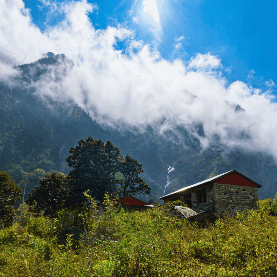 Trekking przez Dolinę Langtang w Nepalu, chatka otoczona skalistymi górami i zieloną roślinnością.