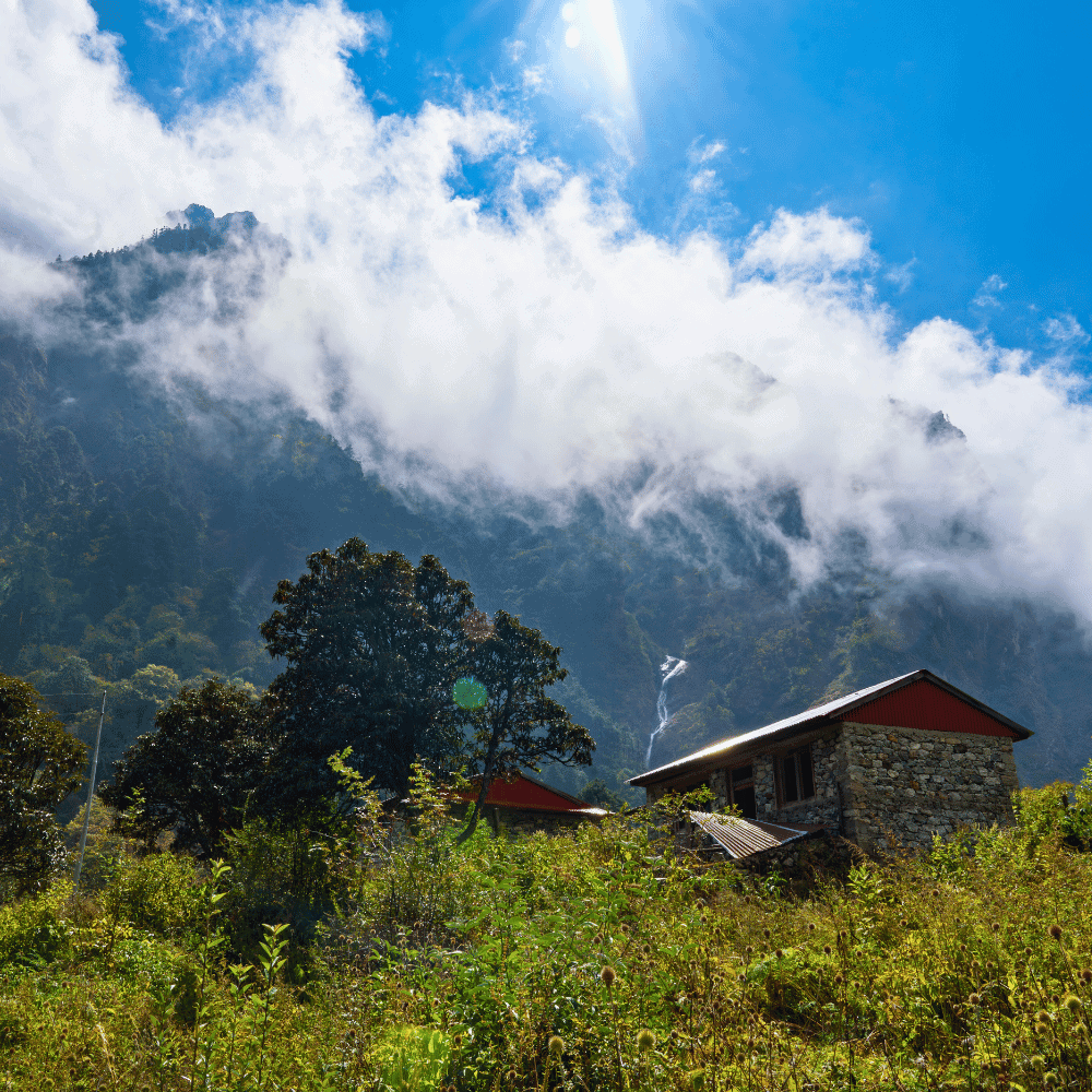Trekking przez Dolinę Langtang w Nepalu, chatka otoczona skalistymi górami i zieloną roślinnością.