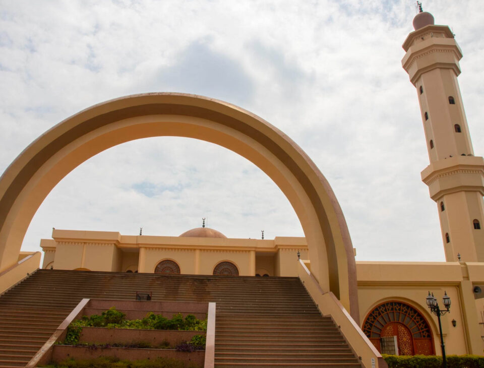 Narodowy Meczet Ugandy w Kampali z jasną fasadą, kopułą i wysokim minaretem, widziany z dołu przez szeroki łuk i schody.