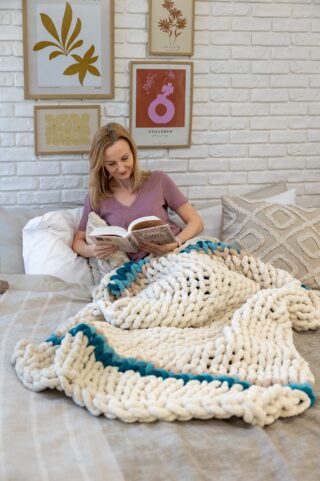 Uczestniczka wyprawy Atma Joga relaksuje się z książką, otulona kocem z wełny stworzonej podczas warsztatów armknittingu.