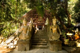 Kamienna brama i schody prowadzące do ukrytej świątyni Pha Lat w Chiang Mai wśród tropikalnej dżungli.