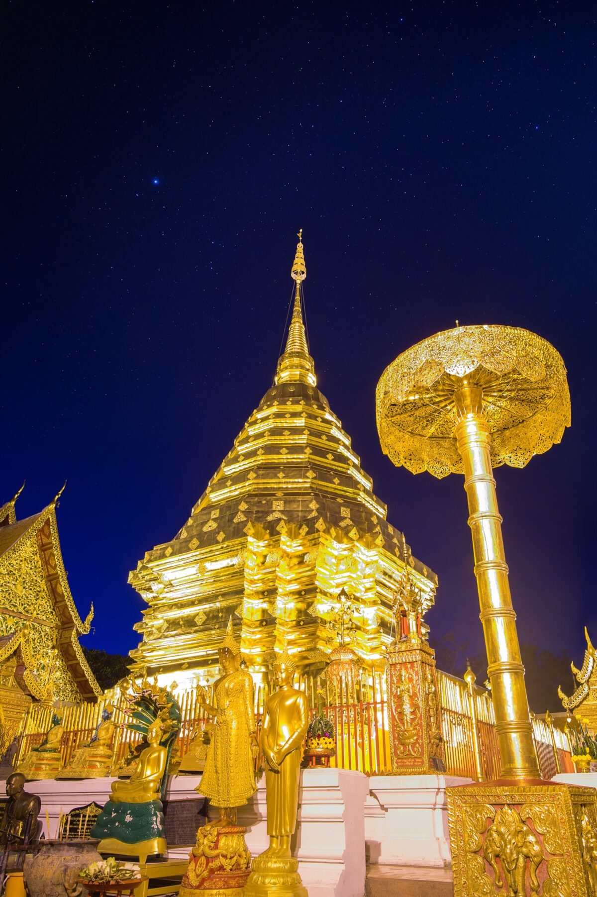 Złota stupia świątyni Wat Phra That Doi Suthep w Chiang Mai oświetlona nocą na tle gwiazd.