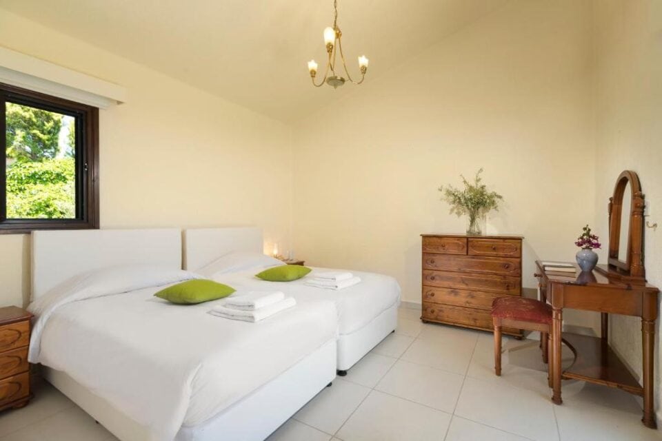 Sypialnia w willi z dwoma osobnymi ł&oacute;żkami, drewnianą toaletką i widokiem na zieleń za oknem.