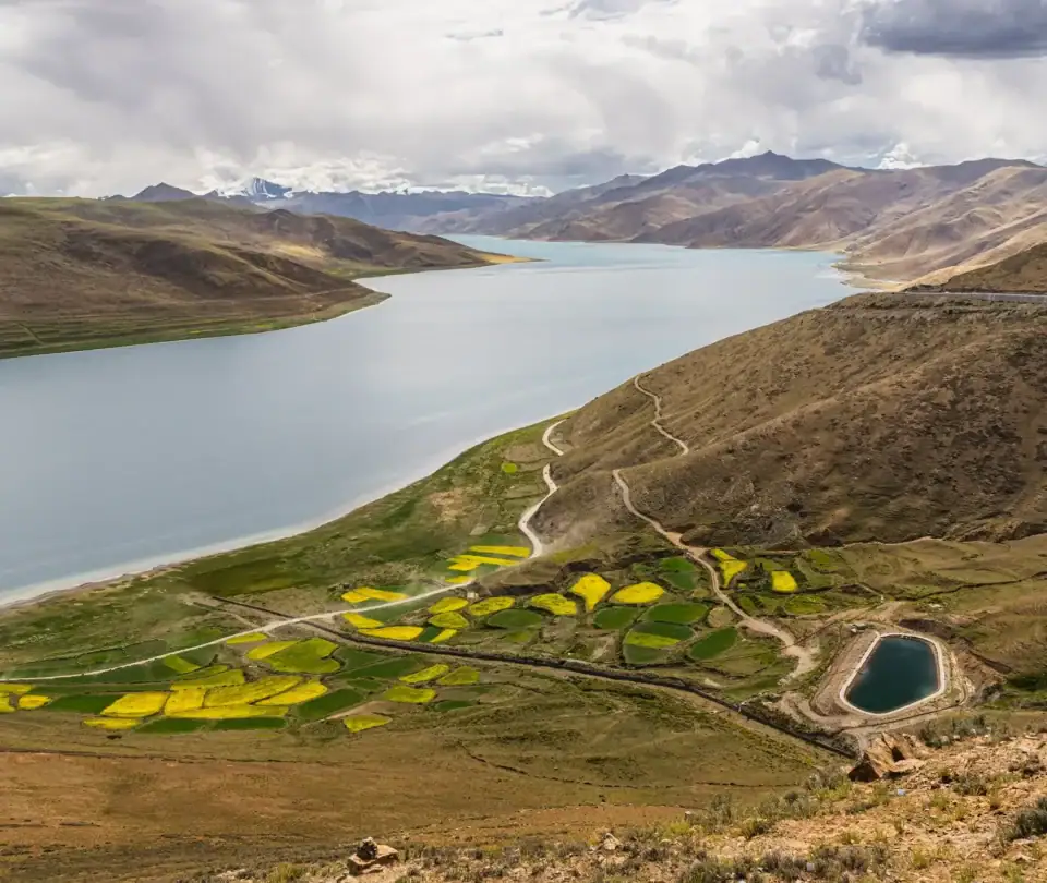 Jezioro Yamdrok widziane z przełęczy Khamba La z polami uprawnymi – jedno z trzech świętych jezior Tybetu