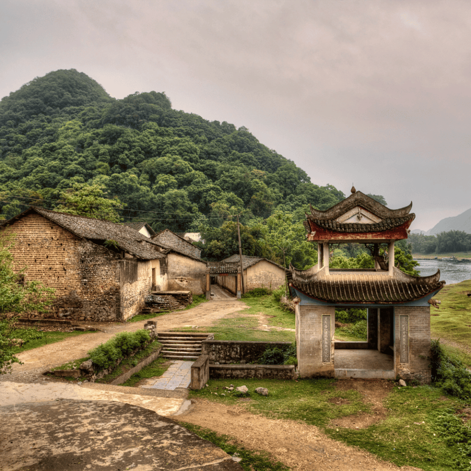Tradycyjna brama w stylu chińskim oraz zabudowania wiejskie w Yangshuo, otoczone zielonymi wzgórzami.