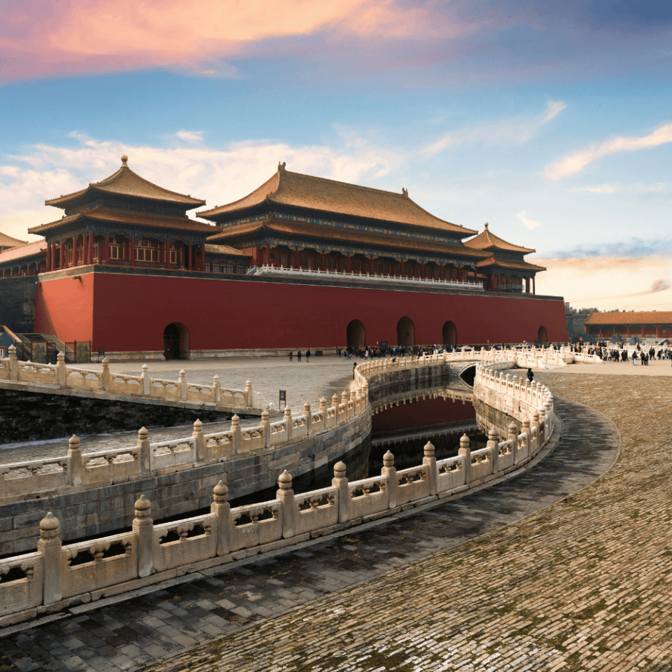 Widok na Zakazane Miasto w Pekinie – monumentalna brama wejściowa, czerwone mury, ozdobne dachy pokryte żółtą dachówką i ozdobne balustrady otaczające kanał wodny pod dziedzińcem, wszystko w świetle zachodzącego słońca.